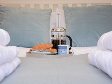 A bed with blue pillows and a tray holding a French press coffee maker croissants and a cup at 2 Pink Cottages Aldeburgh