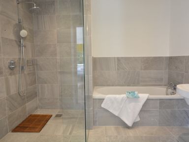 A bathroom with a walk-in shower with wooden mat and a bathtub with towel and soap at 2 Pink Cottages Aldeburgh