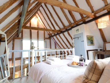 An attic bedroom with exposed wooden beams a metal bed frame a tray with coffee and pastries on the bed at Wassicks Cottage Haughley