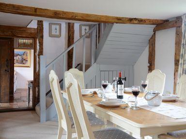 A dining room with a wooden table set with plates wine glasses and a bottle of wine near a staircase at Wassicks Cottage Haughley