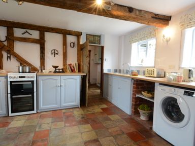 A kitchen with a stove sink washing machine and wooden beams on the ceiling at Wassicks Cottage Haughley