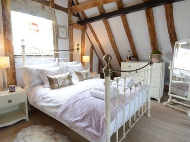 A bedroom with a white metal bed frame wooden beams and a dresser at Wassicks Cottage Haughley