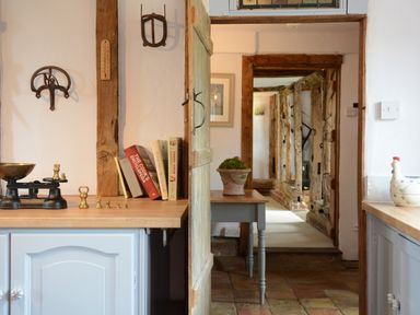 A kitchen counter with a scale, weights, and cookbooks next to a doorway opening to a hallway with wooden beams at Wassicks Cottage Haughley