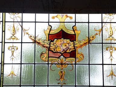 A stained glass window with a decorative crest design including fruits and ornamental scrolls at Wassicks Cottage in Haughley