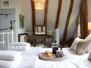A bedroom with a bed with towels and breakfast on a tray and wooden beams on the ceiling at Wassicks Cottage Haughley