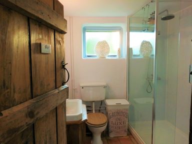 A bathroom with a wooden door a toilet a laundry basket a small sink and a glass shower at Wassicks Cottage in Haughley
