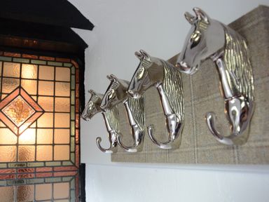 A row of four horse head shaped silver coat hooks mounted on a wall next to a stained glass window at Wassicks Cottage Haughley