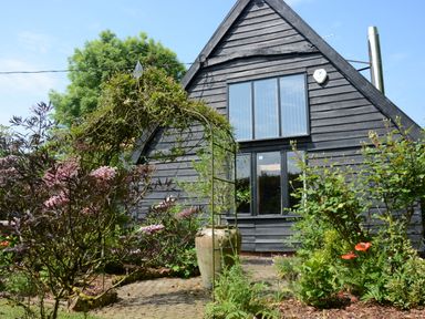 A garden with plants flowers and an archway in front of a black wooden house at Wassicks Cottage Haughley