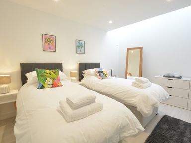 A bedroom with two single beds with white bedding and colorful pillows at Skylight Aldeburgh in Aldeburgh