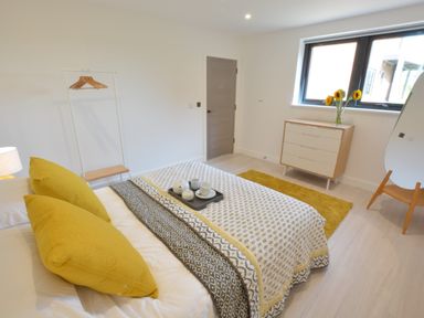 A bedroom with a bed with yellow pillows and patterned bedspread a chest of drawers with a vase of flowers a full-length mirror and a clothes rack at Skylight Aldeburgh in Aldeburgh