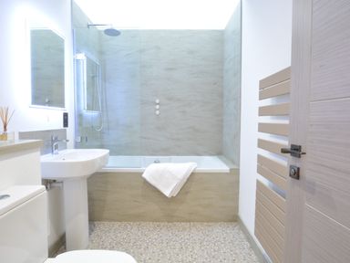 A bathroom with a bathtub shower combo sink toilet and towel on bathtub at Skylight Aldeburgh in Aldeburgh