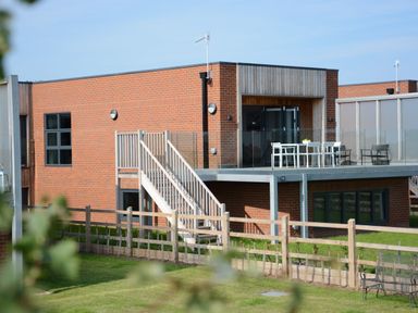 A brick house with stairs leading to a balcony with outdoor furniture and a fenced garden at Skylight in Aldeburgh