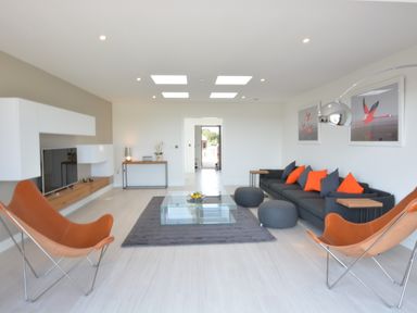 A living room with a black sofa and orange cushions and leather chairs at Skylight Aldeburgh in Aldeburgh