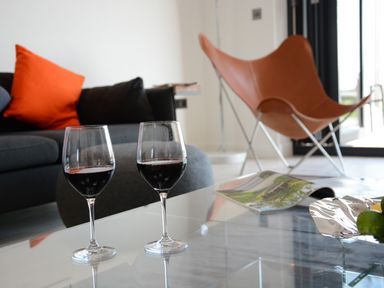 A living room with two glasses of red wine on a glass coffee table and an orange chair in the background at Skylight in Aldeburgh