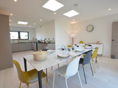 A dining area with a table set for six and an adjoining kitchen in a modern room at Skylight Aldeburgh in Aldeburgh