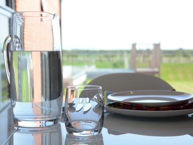 A glass pitcher filled with water and a glass next to a plate with a napkin on a table at Skylight Aldeburgh in Aldeburgh