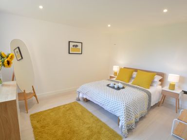 A bedroom with a double bed yellow pillows bedside tables lamps a yellow rug a floor mirror and a wooden dresser at Skylight Aldeburgh in Aldeburgh