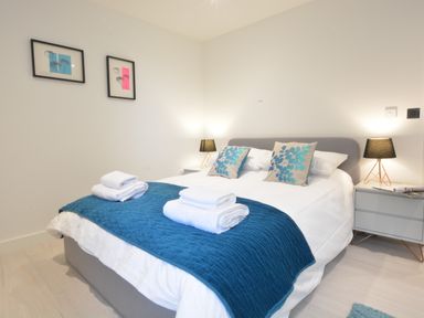A bedroom with a double bed blue throw pillows white towels on bed and bedside tables with lamps at Skylight Aldeburgh in Aldeburgh