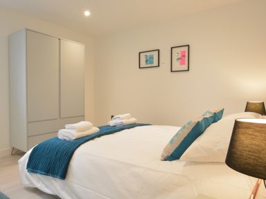A bedroom with a bed, pillows, folded towels, a wardrobe, two framed pictures on the wall, and a lamp at Skylight, Aldeburgh in Aldeburgh