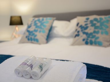 A bed with blue and beige floral pillows and toiletries on white towels at Skylight Aldeburgh in Aldeburgh
