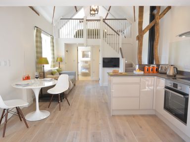 A kitchen and dining area with white table and chairs a sofa and staircase leading to a loft bedroom at Carriage House Bruisyard Near Framlingham