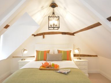 A bedroom with a double bed two bedside tables with lamps and exposed wooden beams at Carriage House Bruisyard Near Framlingham