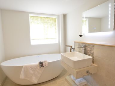 A bathroom with a standalone bathtub towel and book a rectangular sink under a lit mirror at Carriage House Bruisyard Near Framlingham