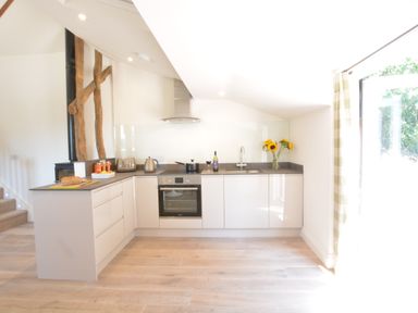 A kitchen with white cabinets black countertop oven and a vase with sunflowers at Carriage House Bruisyard Near Framlingham