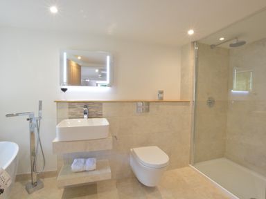 A bathroom with a wall-mounted sink toilet glass shower and freestanding bath at Carriage House Bruisyard Near Framlingham