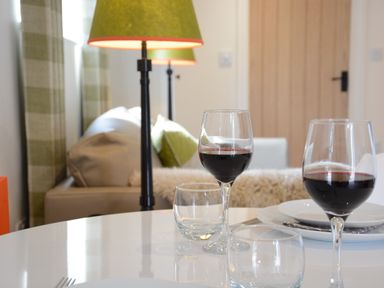 A table with two glasses of red wine and plates in a living room with a sofa and lamps at Carriage House Bruisyard Near Framlingham