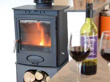 A wood burning stove with fire inside and a bottle of red wine with two glasses on a countertop at Carriage House Bruisyard Near Framlingham