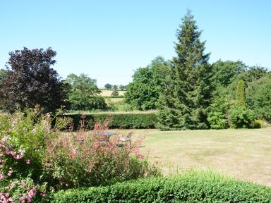 A garden with flowering bushes trees and a metal table with chairs on a lawn at Carriage House Bruisyard Near Framlingham