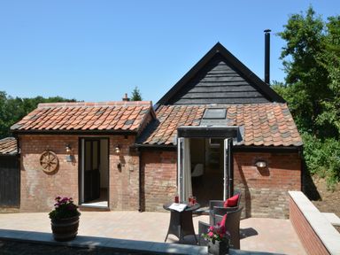 A small brick house with tiled roof and outdoor seating area with table and chairs at Carriage House Bruisyard Near Framlingham