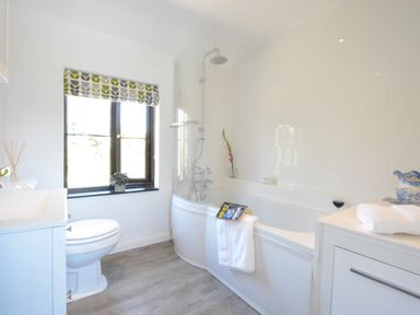 A bathroom with a bathtub shower toilet sink window and a towel at Pine Cottage in Woodbridge