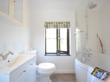 A bathroom with a sink cabinet toilet window and bathtub with shower at Pine Cottage in Woodbridge