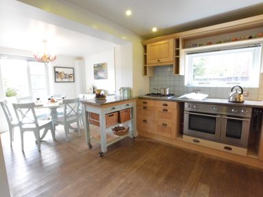 A kitchen with wooden cabinets a dining table with chairs and a mobile island unit at Robert Sadler's Studio in Aldeburgh