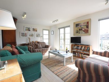 A living room with striped and green sofas a coffee table with wine glasses a TV on a bookshelf and wall art at Robert Sadler's Studio in Aldeburgh