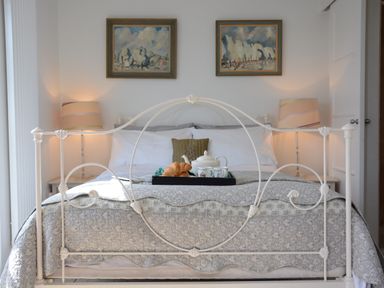 A bedroom with a metal bed frame a tray with a teapot cups and croissants two table lamps and two paintings on the wall at Robert Sadler's Studio in Aldeburgh