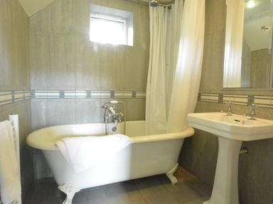 A bathroom with a clawfoot bathtub with a shower curtain and a towel on it and a pedestal sink with a mirror above at Robert Sadler's Studio in Aldeburgh