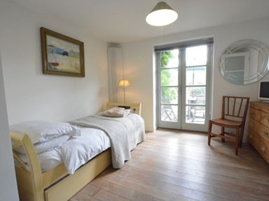 A bedroom with a single bed a wooden chair a wooden dresser and glass doors leading outside at Robert Sadler's Studio in Aldeburgh