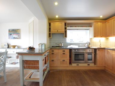 A kitchen with wooden cabinets a stainless steel oven and stove a kitchen island with baskets and a window above the sink at Robert Sadler's Studio in Aldeburgh