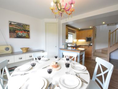 A dining area with a table set for six and an open kitchen with wooden cabinets and stairs at Robert Sadler's Studio in Aldeburgh