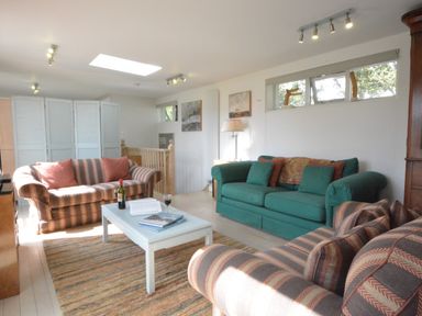 A living room with two striped sofas and one green sofa a white coffee table and paintings on the wall at Robert Sadler's Studio in Aldeburgh