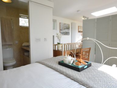 A bedroom with a white metal bed frame a tray with a teapot and croissants on the bed a wooden chair and a folding screen at Robert Sadler's Studio in Aldeburgh