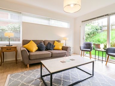 A living room with a sofa holding yellow and gray cushions a coffee table two armchairs and lamps at The Bridge House in Southwold