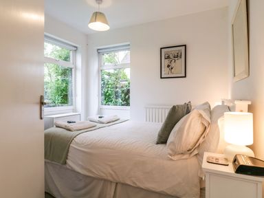 A bedroom with a bed pillows bedside table lamp and windows showing greenery at The Bridge House in Southwold