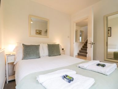 A bedroom with a double bed two green cushions bedside tables lamps mirror and towels at The Bridge House Southwold