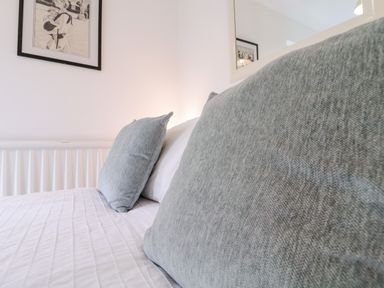 A close up of a bed with gray pillows and white bedding featuring framed artwork on the wall at The Bridge House Southwold