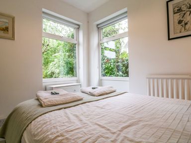 A bedroom with a bed towels on it and two large windows showing greenery outside at The Bridge House Southwold