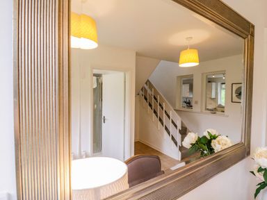 A hallway with stairs and a door reflected in a large wall mirror with flowers on a surface at The Bridge House Southwold